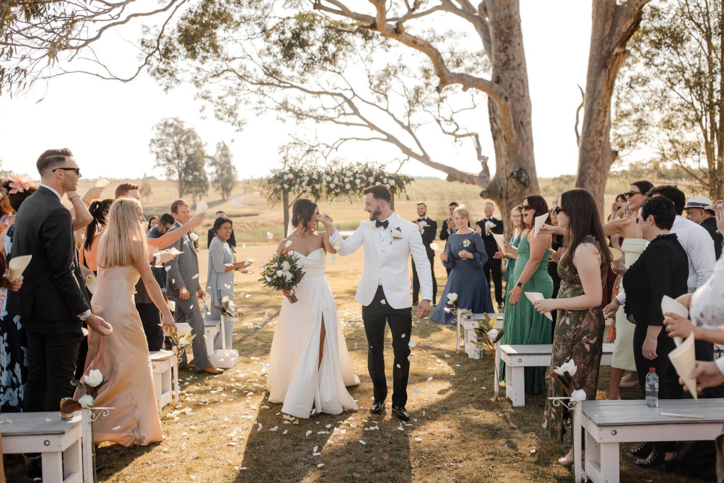 A ceremony under the big gum tree, guests on white benches, the dam behind