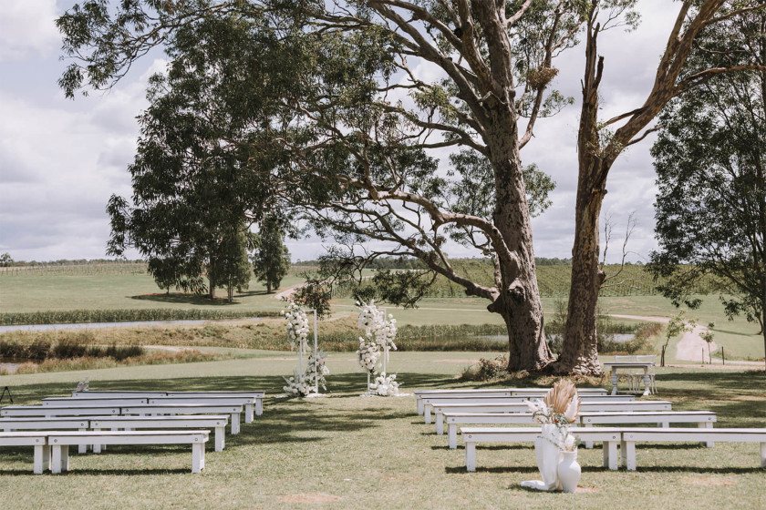 The ceremony set under the gum tree with white benches and an arbour, the dam behind
