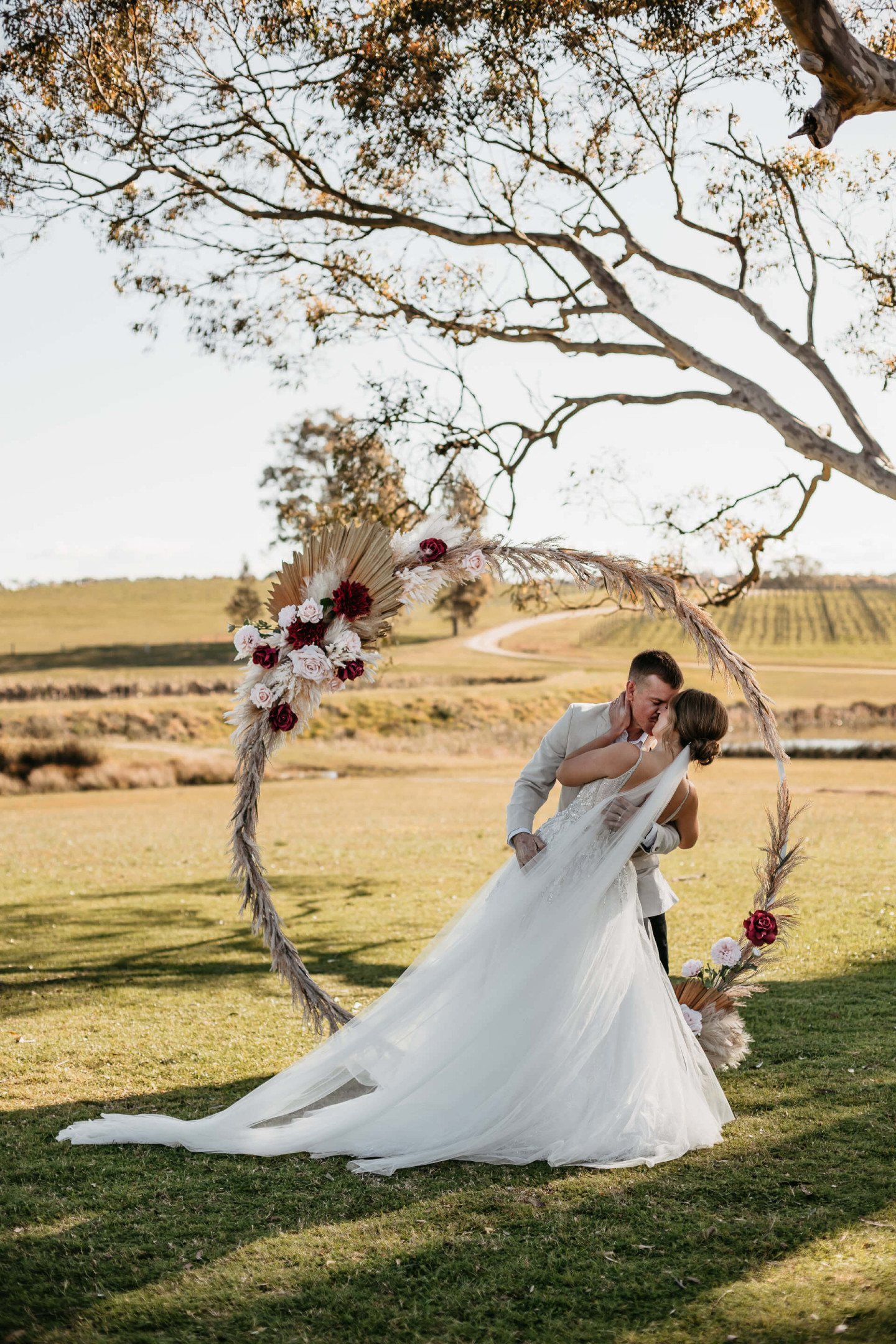 A couple under a circular floral arbour hung from the tree at golden hour